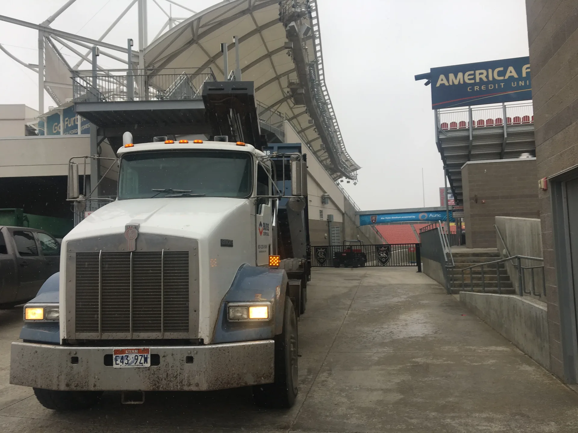 Bubs Disposal hook-lift truck at a stadium construction site with concrete pump truck in background