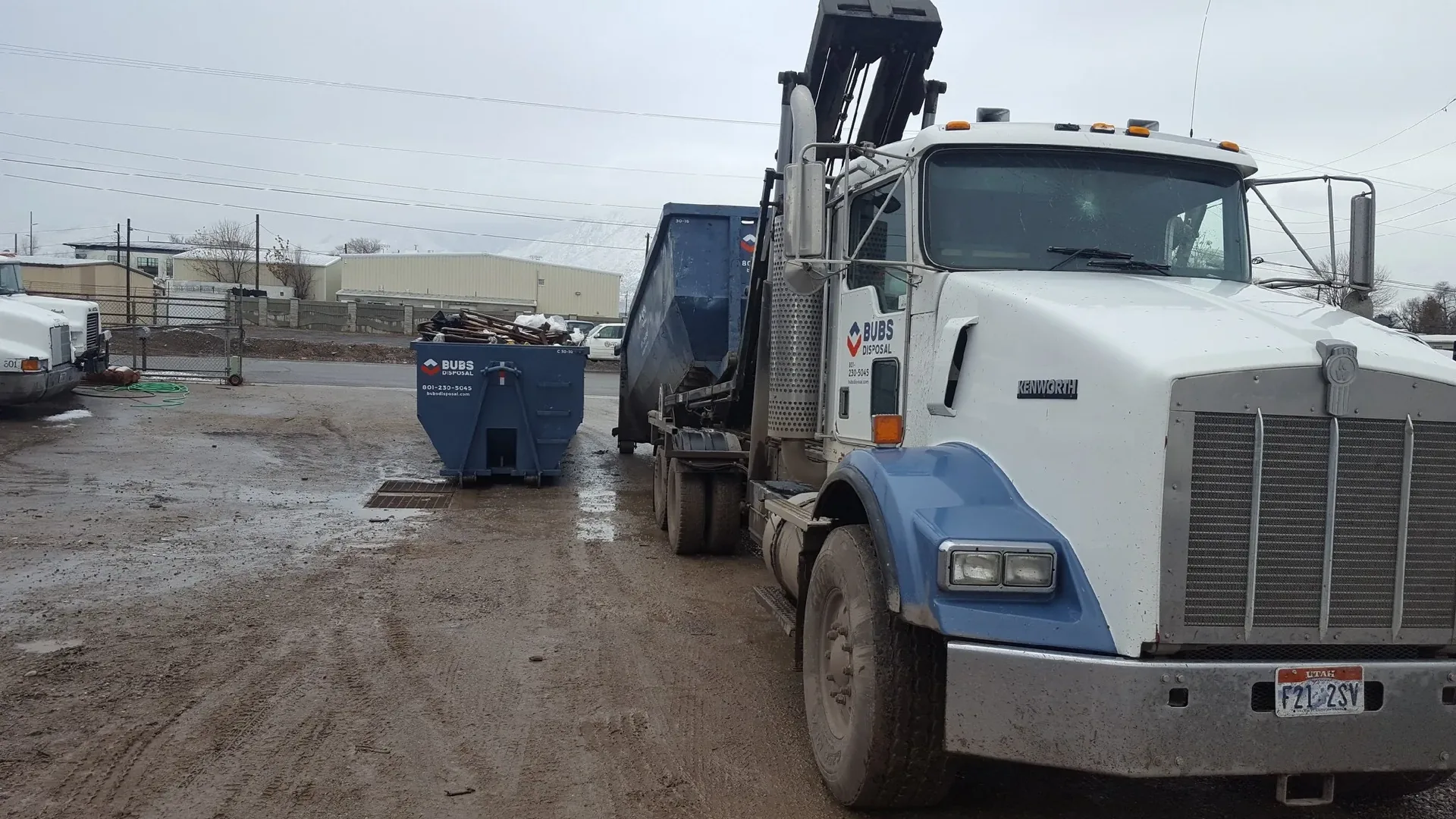 Bubs Disposal Kenworth truck delivering a branded dumpster with snow-capped Wasatch mountains in the background