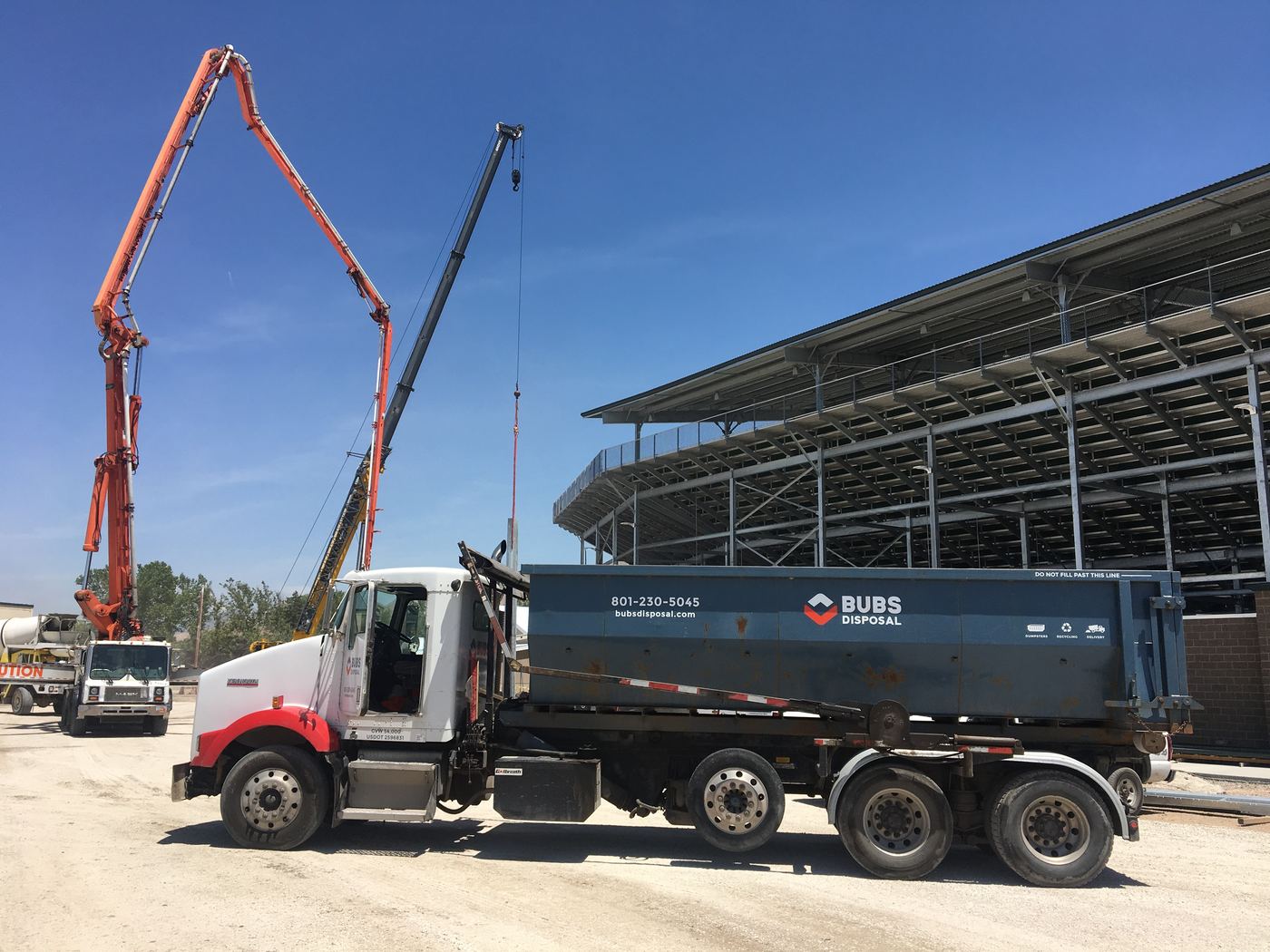 Bubs truck carrying a dumpster at America First Field in Sandy, with two cranes on the stadium job